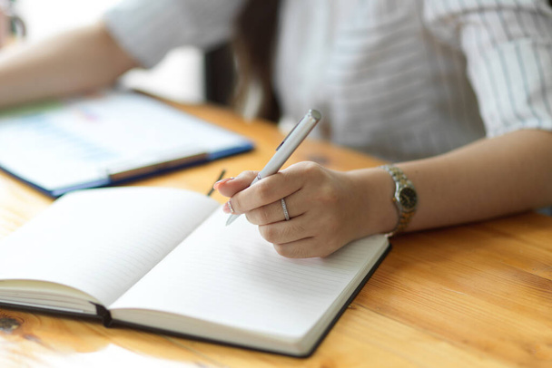 Крупным планом, деловая женщина пишет бизнес-стратегию на ноутбуке в офисе, пустой блокнот, держит ручку, делает заметки, организует повестку дня - Фото, изображение