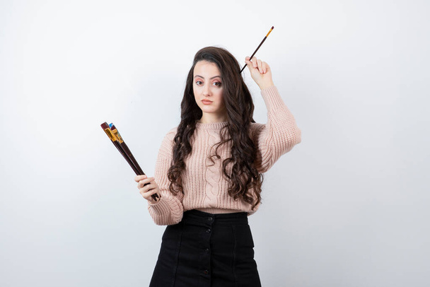 Picture of a talented artist-girl holding paintbrushes against white wall . High quality photo - Photo, Image