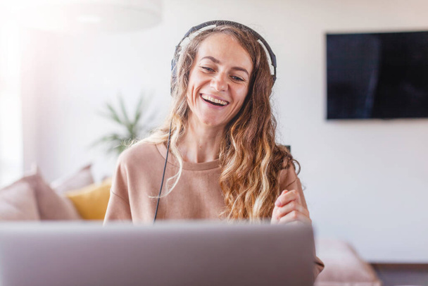 Smiling girl wearing headphones using laptop, looking at screen, happy young woman listening to favorite music while have video chat,  female learning webinar    - Photo, image