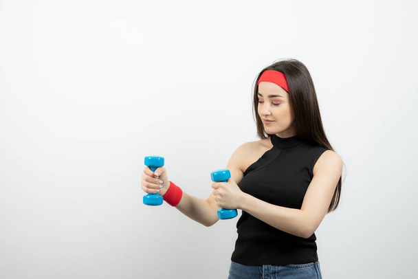 Young fitness woman holding blue dumbbells against white wall . High quality photo - Photo, Image
