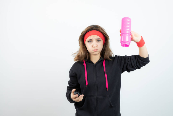 Фотографія молодої спортивної дівчини, що тримає рожеву пляшку води. Високоякісна фотографія
 - Фото, зображення