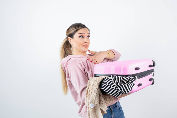 Zdjęcie młodej modelki trzymającej niechlujną walizkę podróżną. Wysokiej jakości zdjęcie - Zdjęcie, obraz