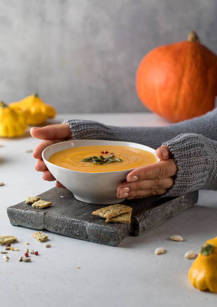 A bowl of warm pumpkin soup with seeds in your hands. Comfortable riding. Vegetarian dishes. - Fotografie, Obrázek