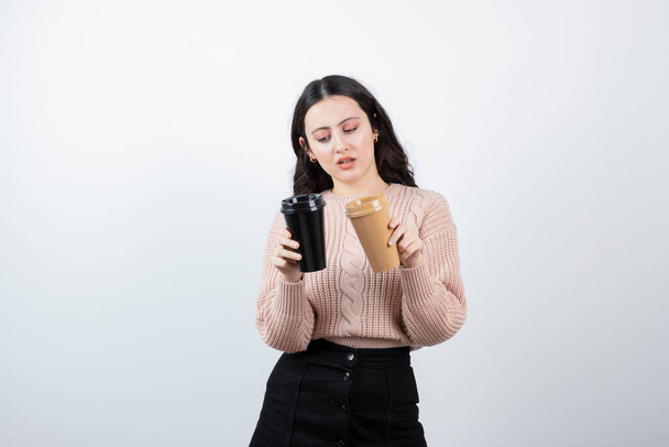 Muotokuva nätistä tytöstä, jolla on kaksi kuppia juomaa valkoista seinää vasten. Laadukas kuva - Valokuva, kuva