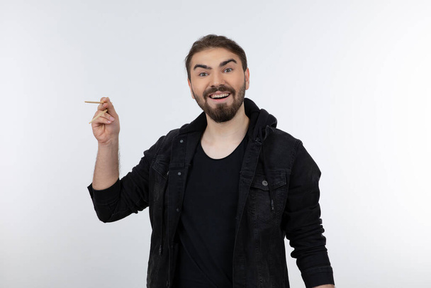 Portrait photo of a young bearded man in black outfit holding disposable chopsticks . High quality photo - Foto, afbeelding