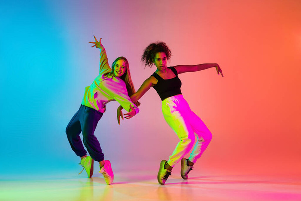 Two beautiful stylish hip-hop dancers on colorful gradient background in neon lights - Фото, изображение