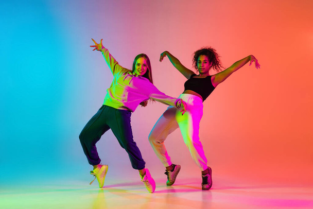 Expresión. Dos hermosas bailarinas de hip-hop con estilo sobre fondo degradado colorido en luces de neón - Foto, Imagen