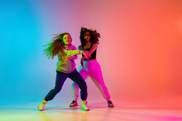 Zwei schöne stylische Hip-Hop-Tänzer auf farbenfrohem Gradienten-Hintergrund im Neonlicht - Foto, Bild
