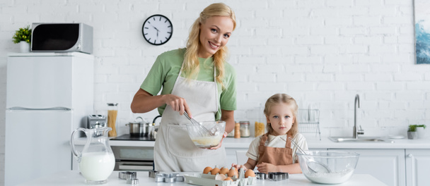 usmívající se matka míchání přísady v misce při vaření s dcerou v kuchyni, banner - Fotografie, Obrázek