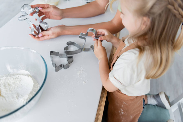 mujer mostrando cortador de galletas a hija borrosa en la cocina - Foto, imagen