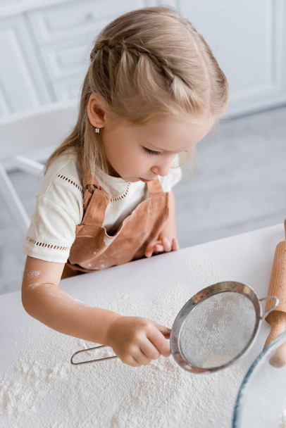 bambina setacciando farina sul tavolo della cucina - Foto, immagini