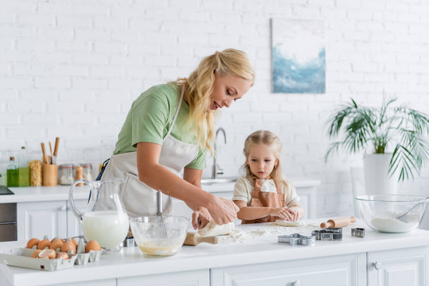 женщина показывает сырое тесто дочери на кухне - Фото, изображение