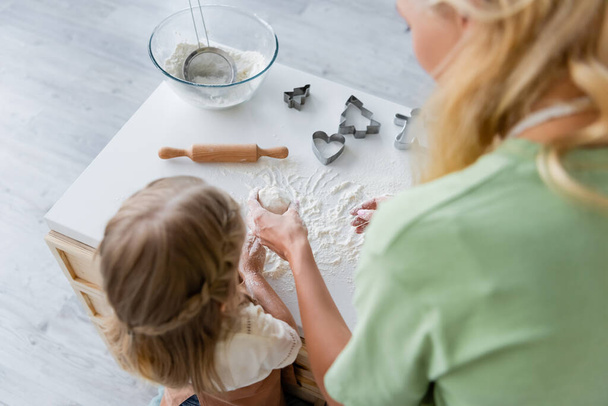 overhead view of blurred woman showing dough to daughter in kitchen - Photo, Image