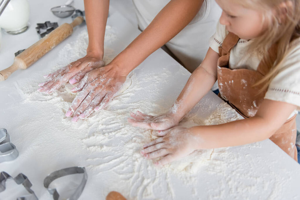 high angle view of mom and blurred daughter kneading dough in kitchen - Foto, imagen