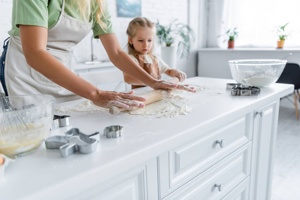 woman with daughter rolling raw dough in kitchen - Φωτογραφία, εικόνα