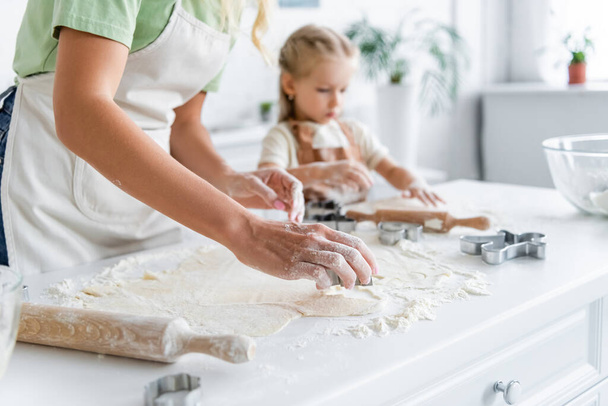 woman cutting dough with cookie cutter near blurred child in kitchen - Foto, immagini