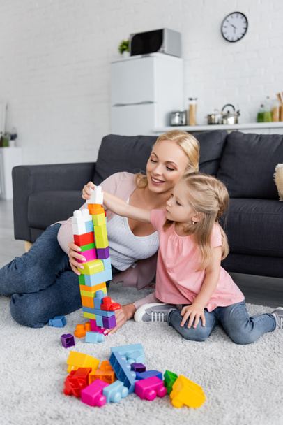 girl making tower of colorful building blocks near happy mom - Photo, Image