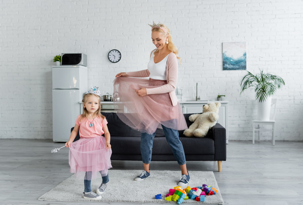 cheerful woman and child in costumes of princesses dancing in kitchen - Photo, Image