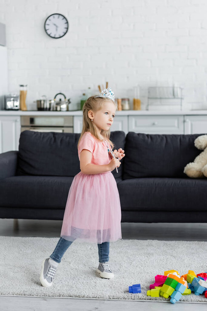 girl in toy crown and tulle skirt standing with magic wand at home - Valokuva, kuva