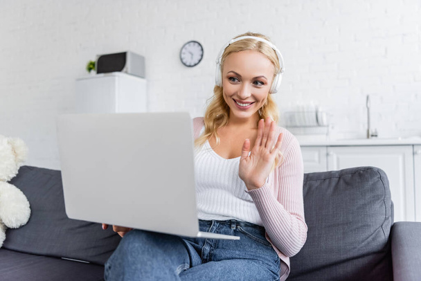 cheerful woman in headphones waving hand during video chat on laptop - Photo, Image