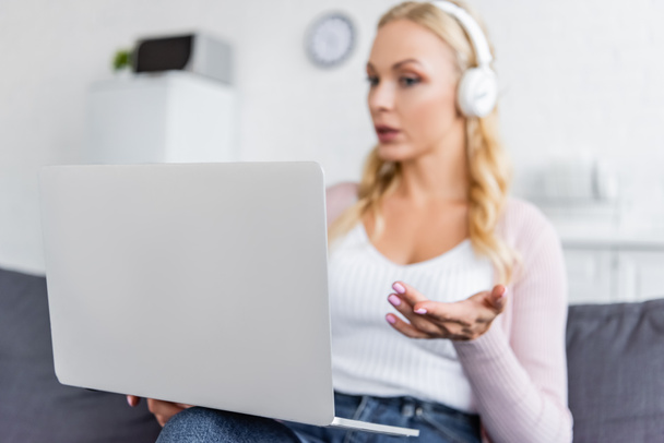blurred woman in headphones pointing with hand at computer during video call - Foto, imagen