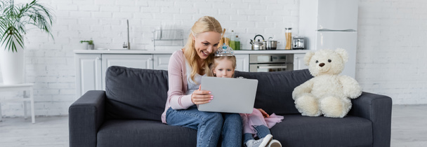 onnellinen nainen tytär lelu kruunu istuu sohvalla kannettava tietokone, banneri - Valokuva, kuva