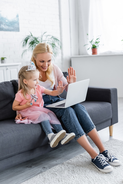 cheerful woman and girl in toy crown waving hands during video call on laptop - Fotoğraf, Görsel