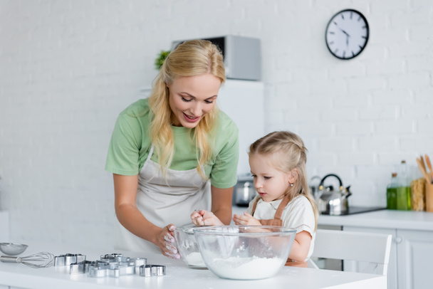 niña cribando harina en un tazón mientras cocina con mamá en la cocina - Foto, Imagen