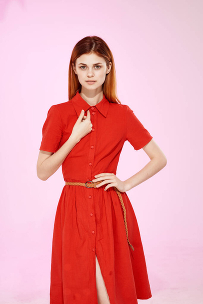 rudowłosa kobieta w czerwonej sukience pozująca na różowym tle. Wysokiej jakości zdjęcie - Zdjęcie, obraz