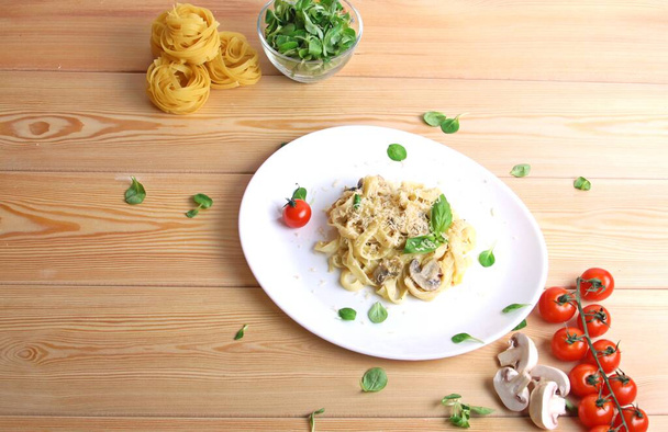 Keitetty italialainen Fettuccine juustolla, sienillä, tomaateilla, basilikalla, levyllä ja kypsentämättömällä pastalla puisella taustalla. Ylhäältä. - Valokuva, kuva