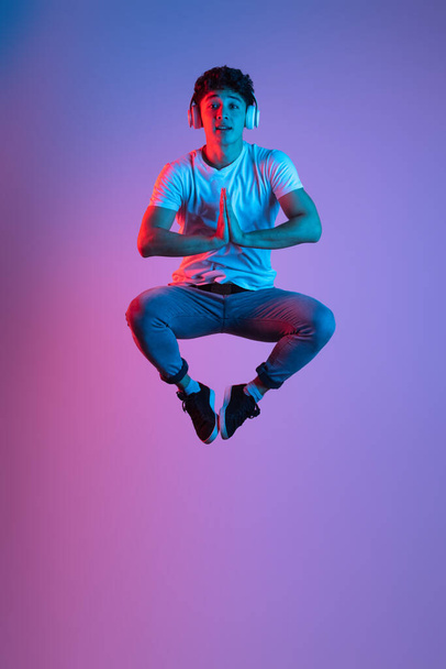 Stylish young asian man isolated over lilac color studio background in pink neon light. Concept of human emotions, fashion, beauty, youth - Fotó, kép