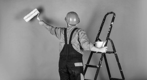 thermal insulation works. Painter man staircase. To make repairs. man in working clothes painting wall in empty room. painter in overall and cap with paint bucket. builder worker painting facade - Fotoğraf, Görsel