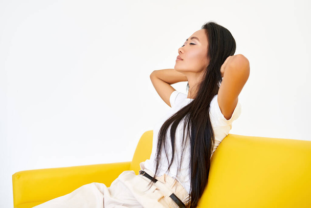 Young pretty woman closed her eyes sitting on yellow sofa and relaxing after busy day - 写真・画像