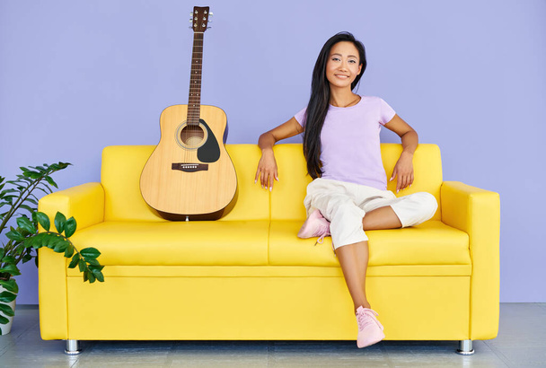 Pretty woman with guitar sitting on comfortable sofa - Fotografie, Obrázek