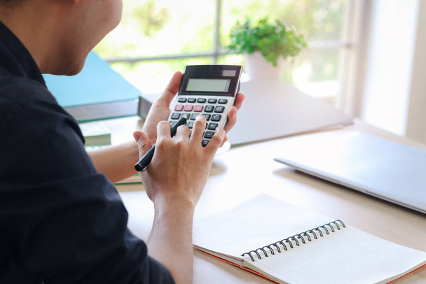Un homme d'affaires ou un comptable asiatique jeune homme tenant calculatrice pour calculer les données financières, le coût et le budget sur place à la maison, statistiques comptables et analyste de crédit pour le paiement. - Photo, image