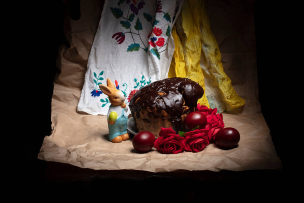 Gyönyörű húsvéti háttér. Csokoládé torta színes tojással és húsvéti nyuszi a háttérben egy hímzett ing. - Fotó, kép