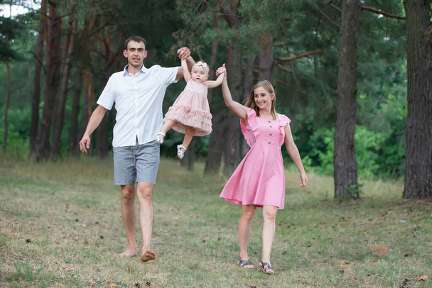 Чоловік, дружина та їхня маленька донька для прогулянки в парку. Щасливий тато і мама викидають свою маленьку смішну однорічну доньку
. - Фото, зображення