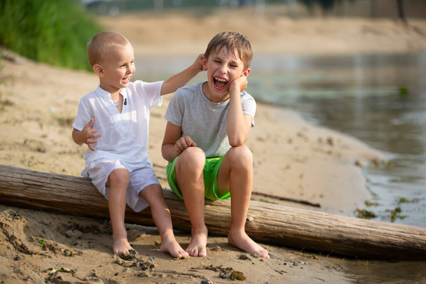 Deux frères, l'aîné et le plus jeune, jouent au bord de la rivière. Les enfants sur la rive sablonneuse parlent et se livrent. - Photo, image