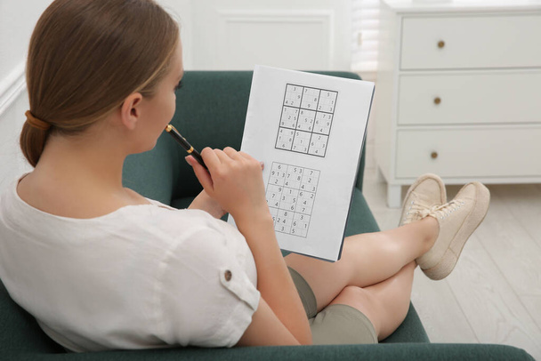 Young woman solving sudoku puzzle on sofa indoors - Fotoğraf, Görsel