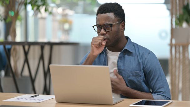 African Man Coughing while using Laptop in Modern Office  - 写真・画像