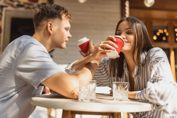 Zugeschnittenes Porträt eines jungen schönen Paares, das an einem strahlenden Sommertag im Café sitzt und draußen gemeinsam Kaffee genießt - Foto, Bild