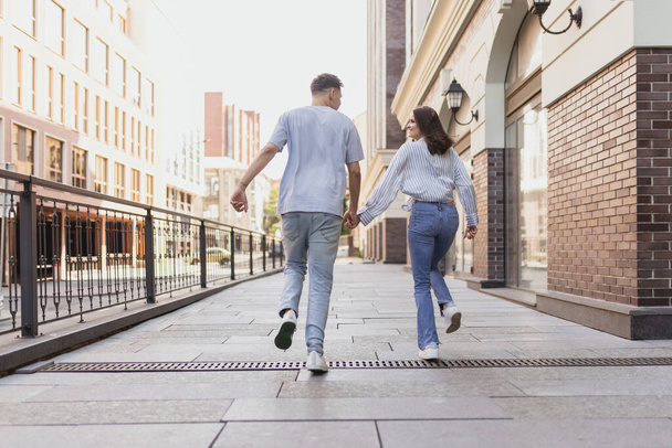 Retrato de larga duración por detrás de una joven pareja feliz caminando por la ciudad en un día soleado de verano - Foto, Imagen