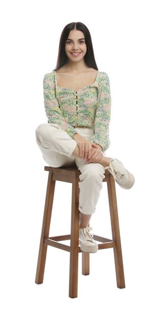 Beautiful young woman sitting on stool against white background - Valokuva, kuva