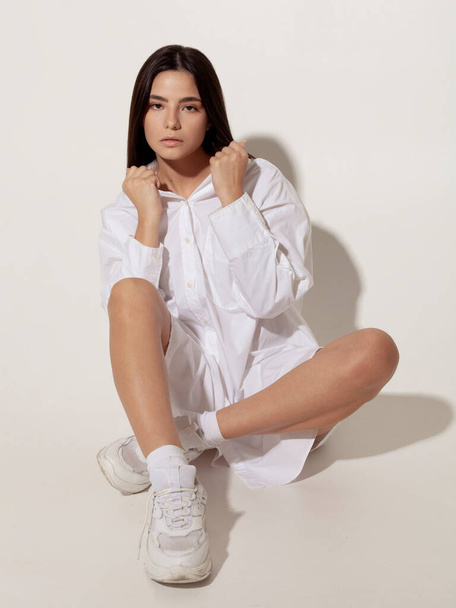 beautiful brunette in a white shirt sits on the floor - Фото, зображення