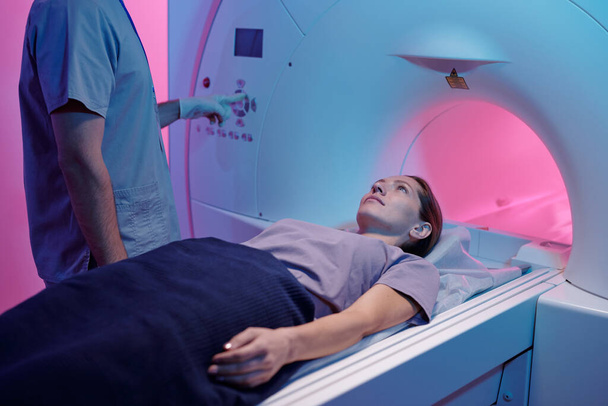 Νεαρή γυναίκα στο ιατρικό τραπέζι κινείται στο μηχάνημα μαγνητικής τομογραφίας - Φωτογραφία, εικόνα