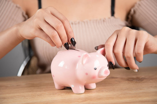 uma mulher coloca uma moeda em um banco porquinho - Foto, Imagem
