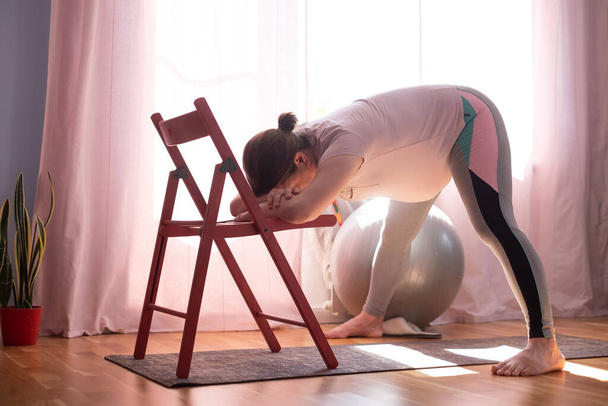 Zwangere vrouw doet inversie Standing Intense Spread Leg Prasarita Padottanasana yoga pose thuis - Foto, afbeelding