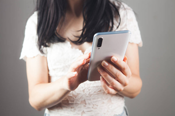 fiatal nő nyomja meg a telefon képernyőjén egy szürke háttér - Fotó, kép