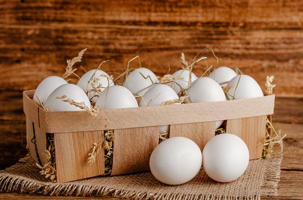 Huevos de pollo blanco en un recipiente de madera con heno. Copiar espacio. - Foto, Imagen