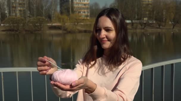 Девушка держит клубок пряжи и крючок во время фотосессии на набережной в городе  - Кадры, видео